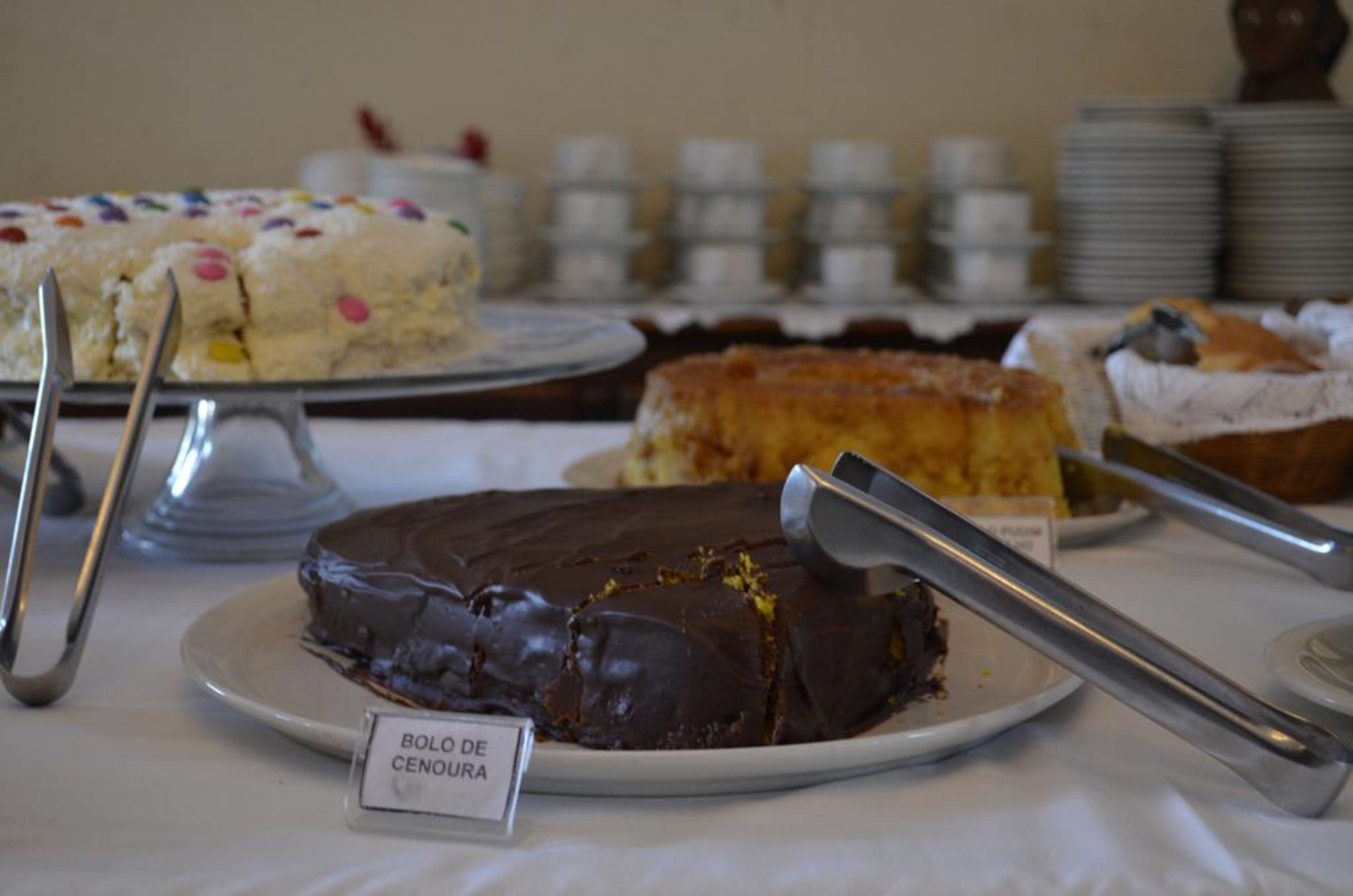 Una exhibición de postres con varios pasteles y un letrero que indica un pastel de chocolate llamado 'Bolo de Cenuça'.