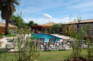 A pool area with lounge chairs, a palm tree, and a building with a tiled roof. - Vila Real Hotel (Jau)