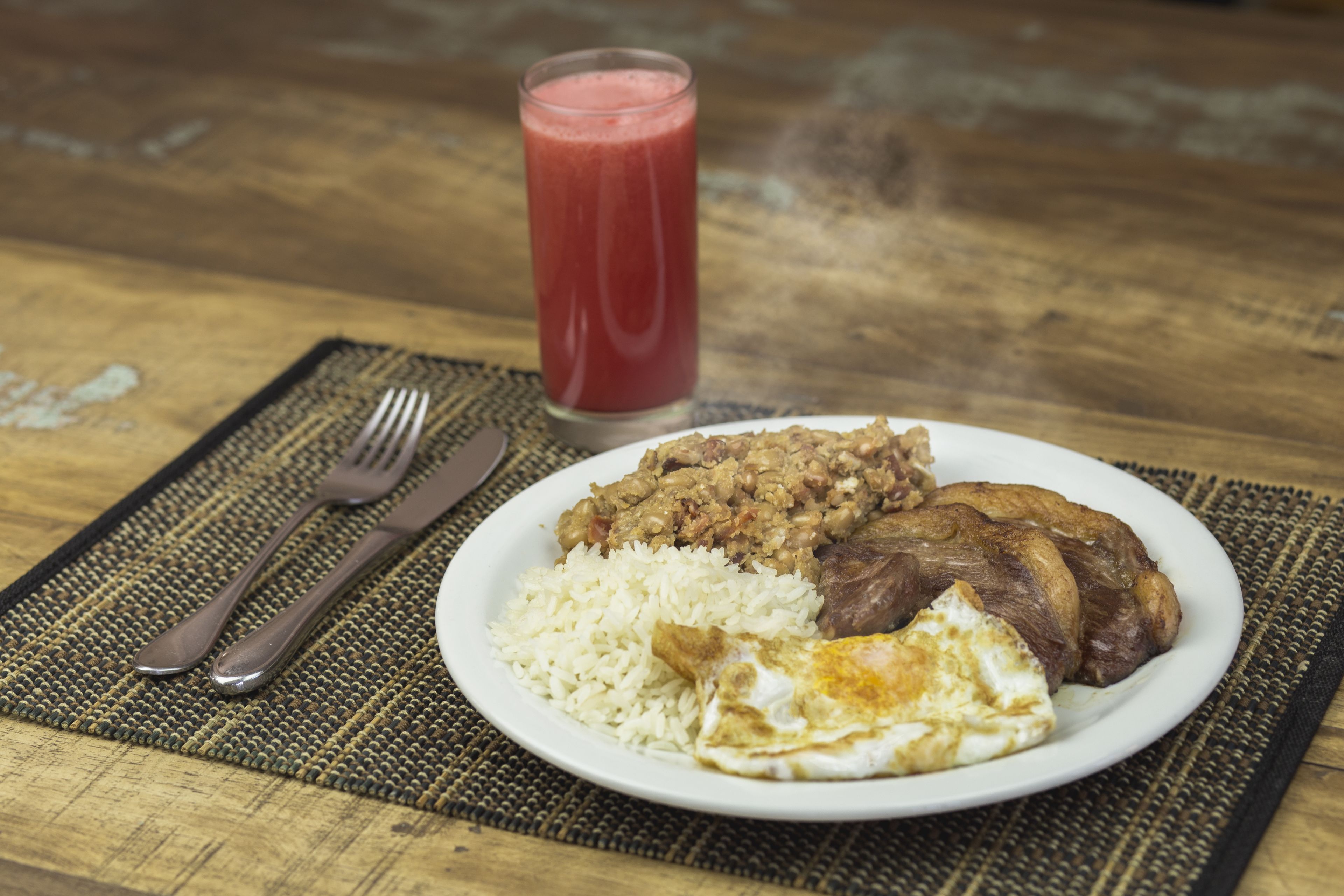 A plate with rice, beans, meat, and an egg on a table with a fork and knife.