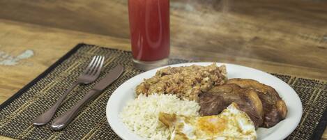 A plate with rice, beans, meat, and an egg on a table with a fork and knife.