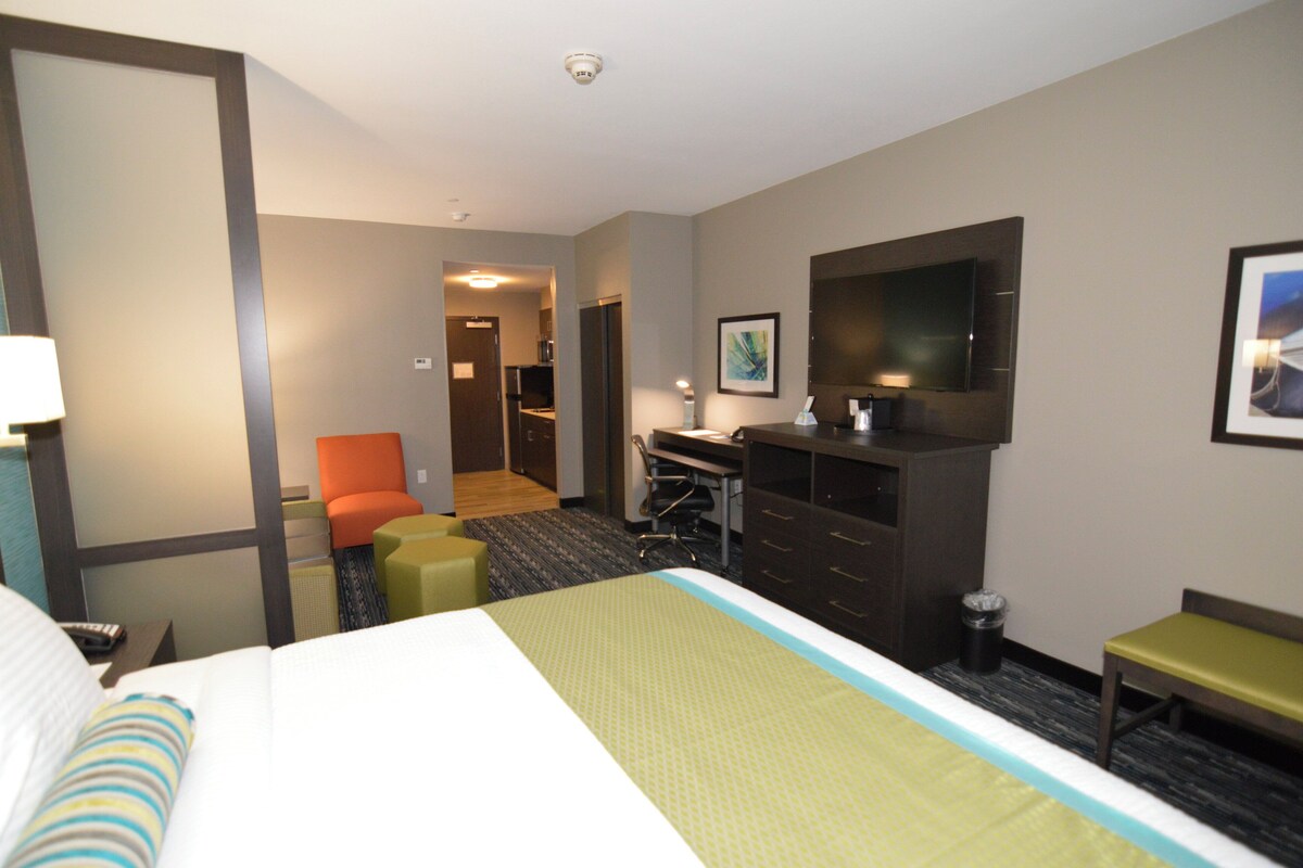 A hotel room with a bed, a desk, a chair, a TV, and a small kitchenette.