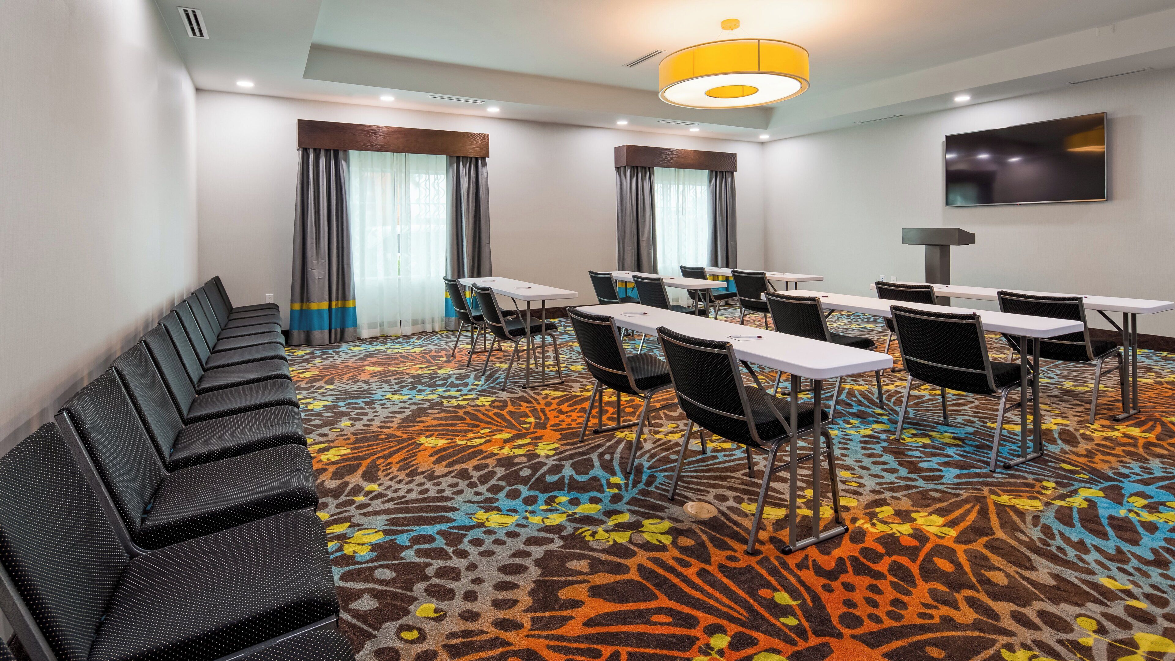 A conference room with a patterned carpet, white tables, and black chairs.