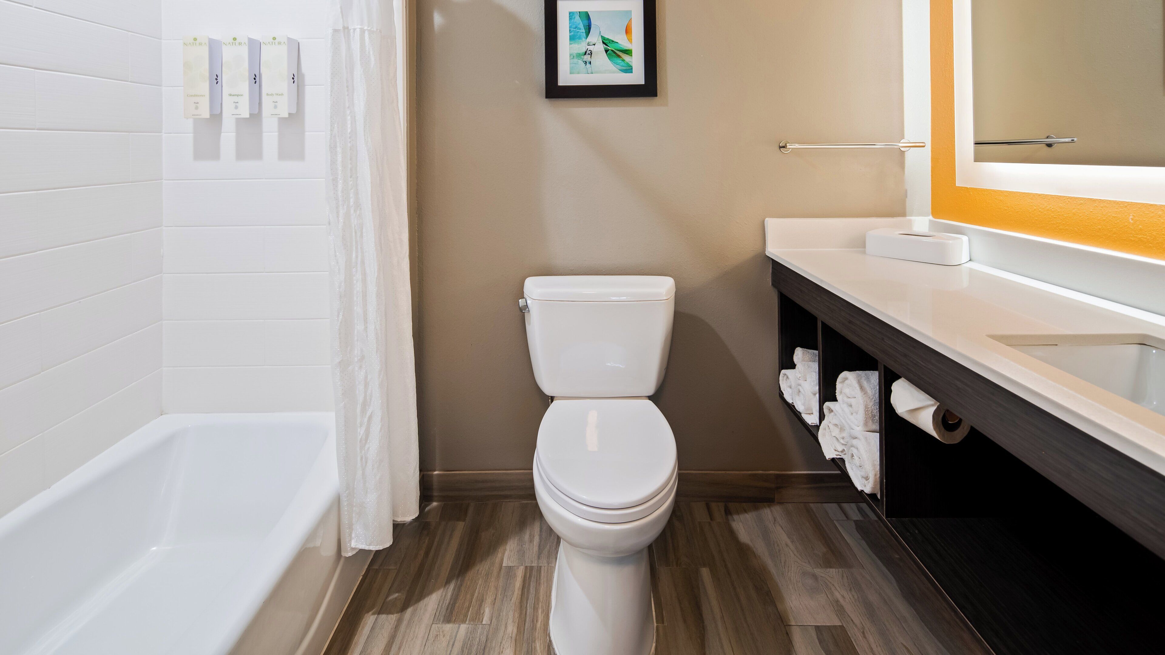 A modern bathroom with a white toilet, a bathtub, and a vanity with a mirror.