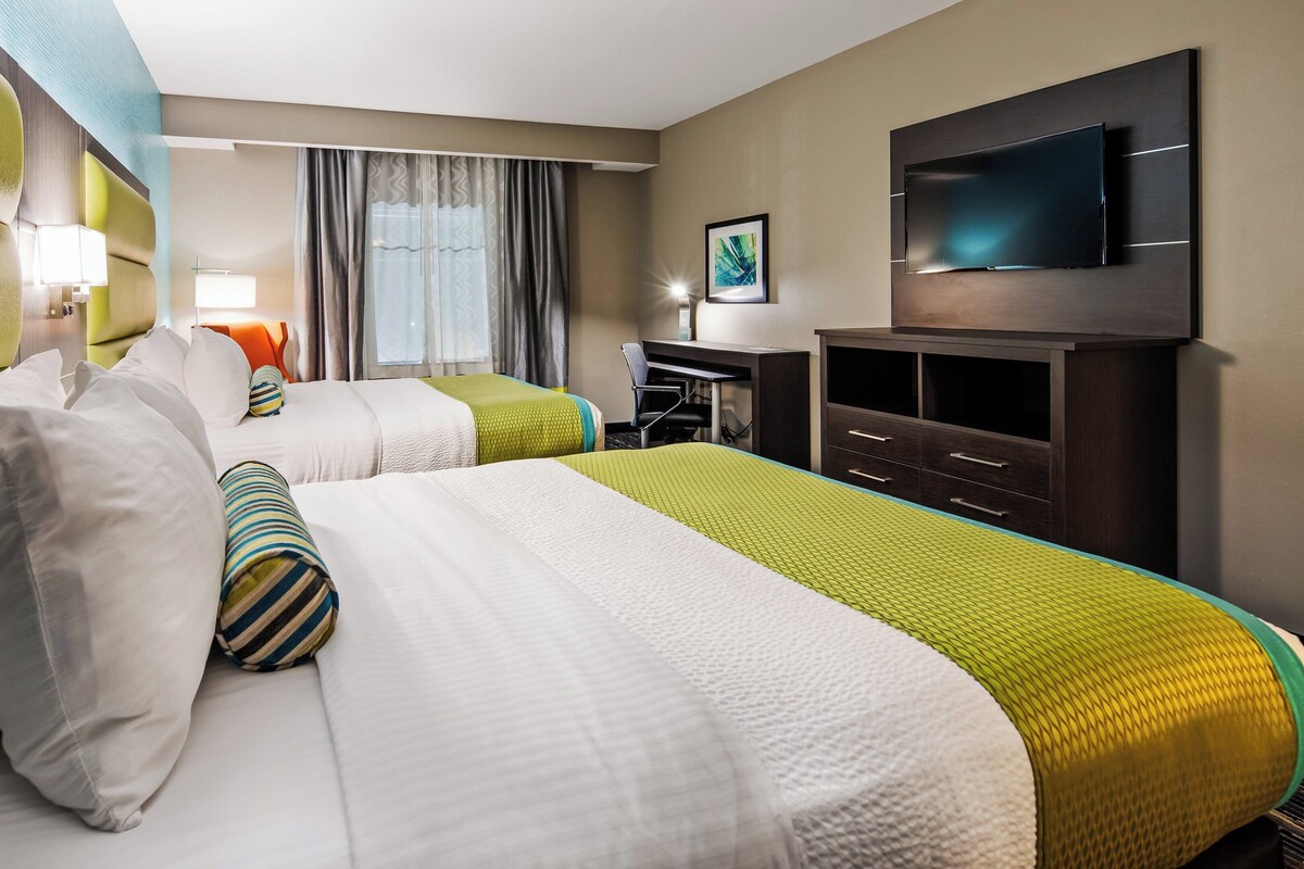 A hotel room with two beds, a desk, a TV, and a window with curtains.