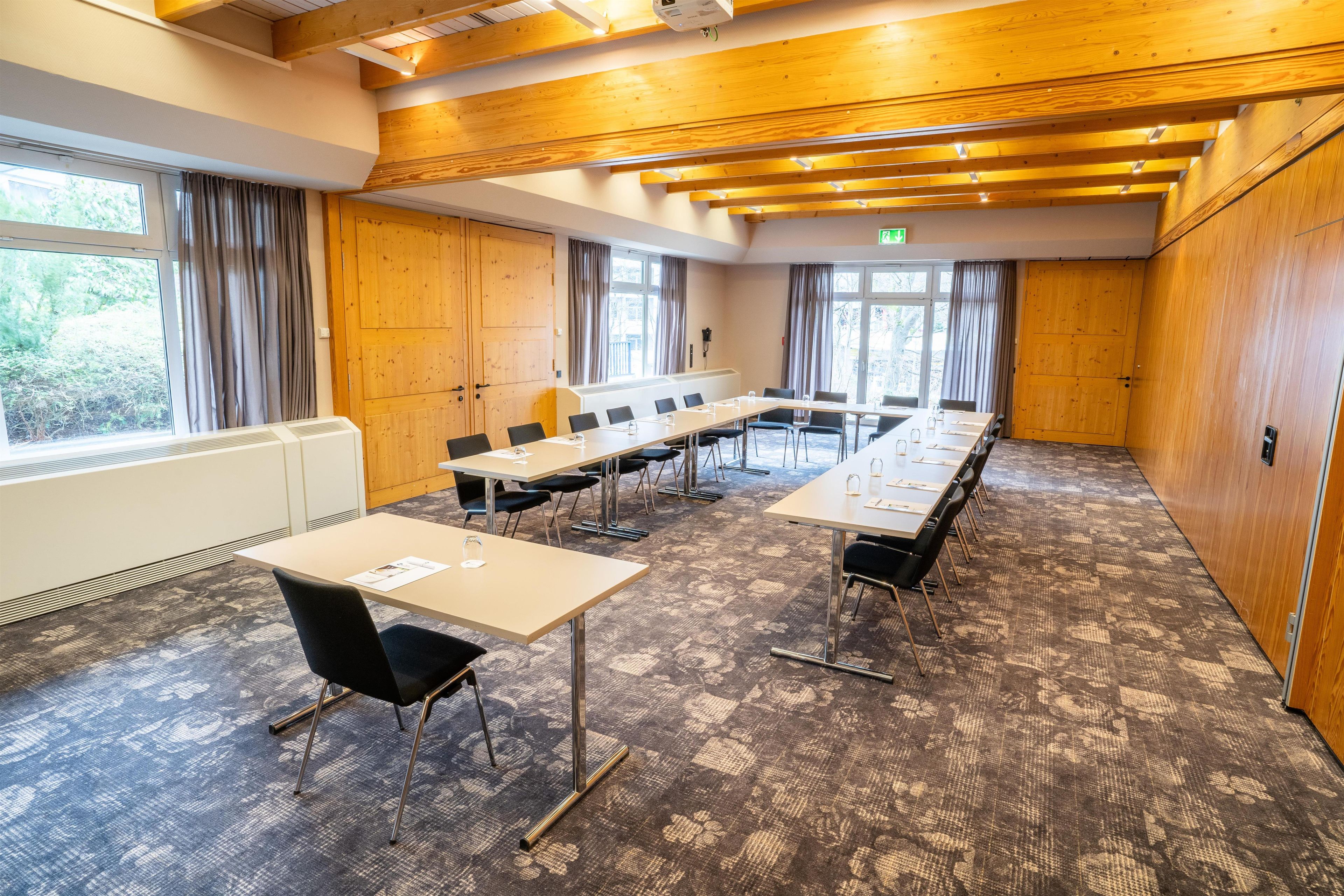 Une salle de conférence dotée de longues tables, de chaises et offrant une vue sur l’extérieur grâce à de grandes fenêtres.