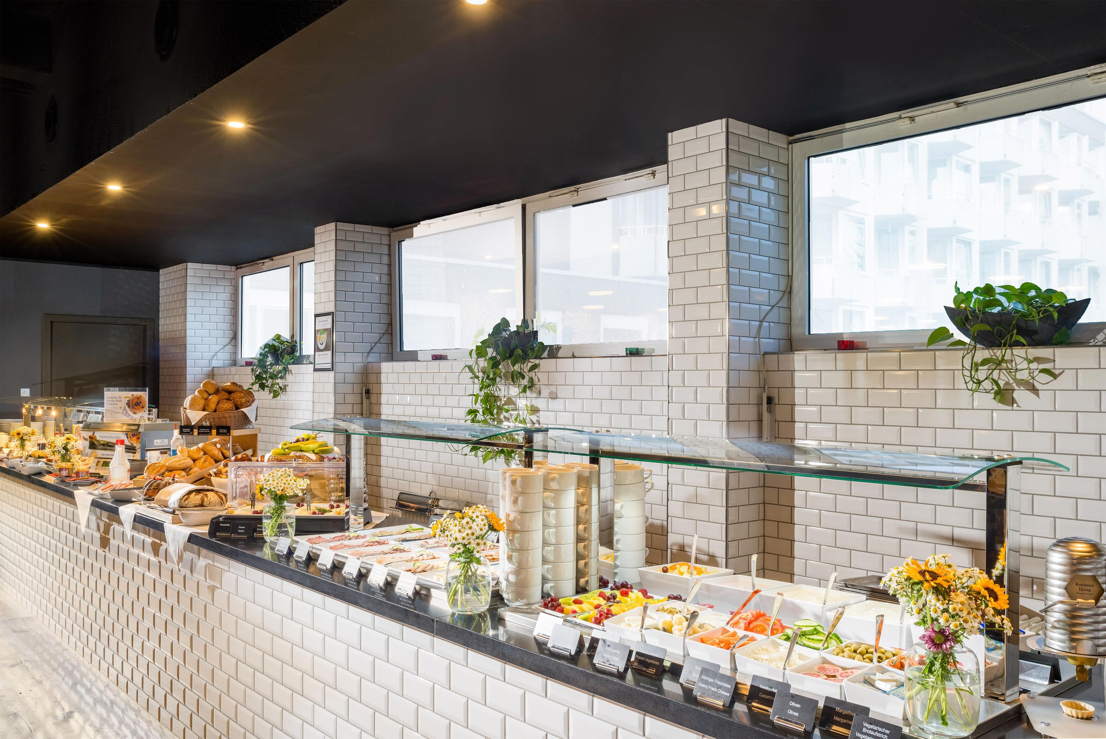 Zona de bufé con diversas opciones de comida, una vitrina de vidrio y una pared de ladrillo con ventanas.