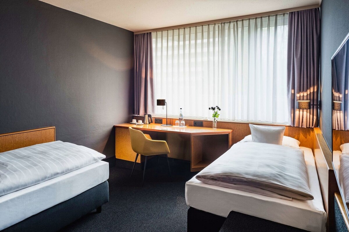 A hotel room with two beds, a desk, and a chair.
