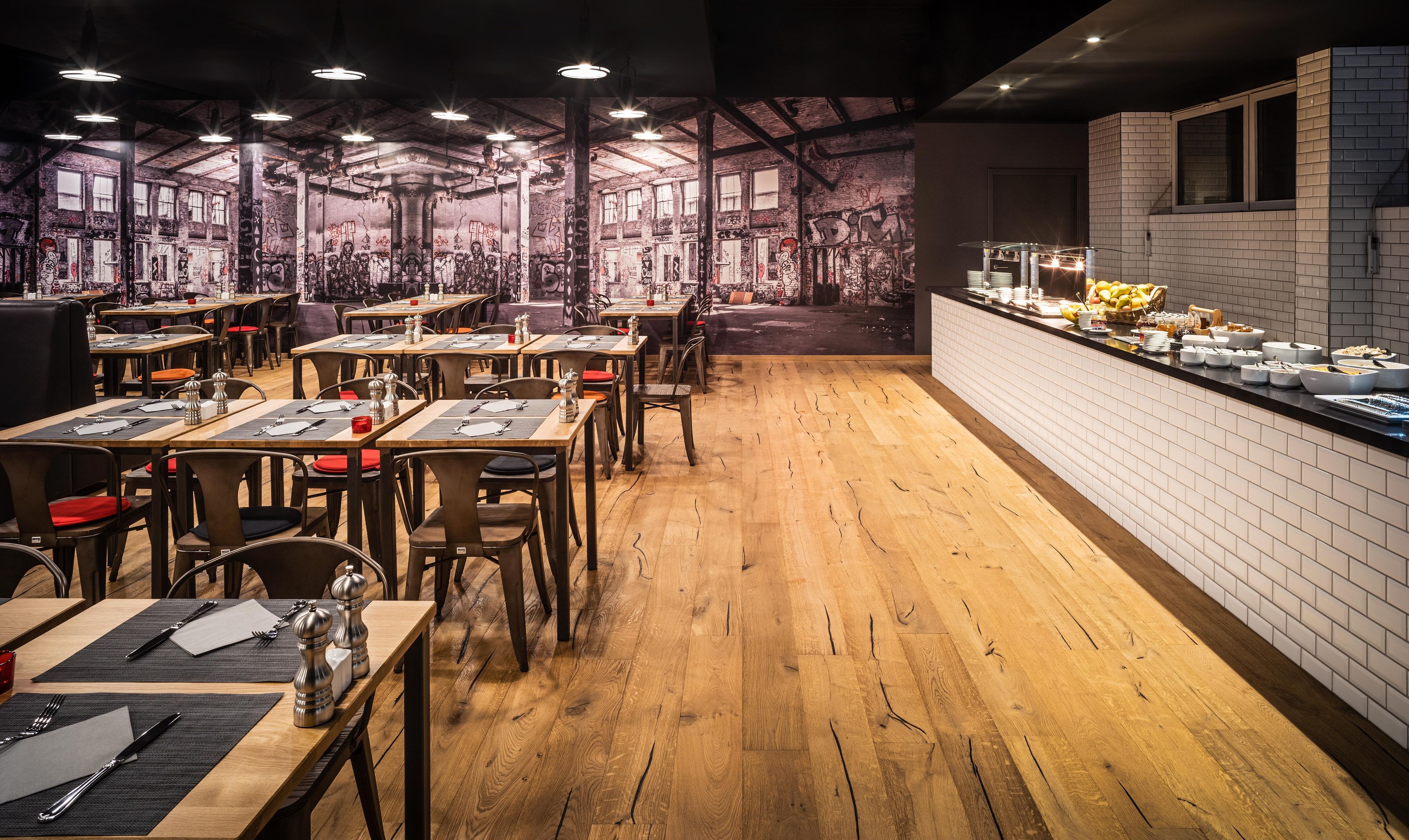 A restaurant with wooden flooring, tables set with cutlery, and a buffet counter.