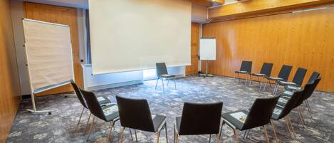 Una sala de conferencias con piso alfombrado, paredes de madera, una pantalla blanca y una pizarra.