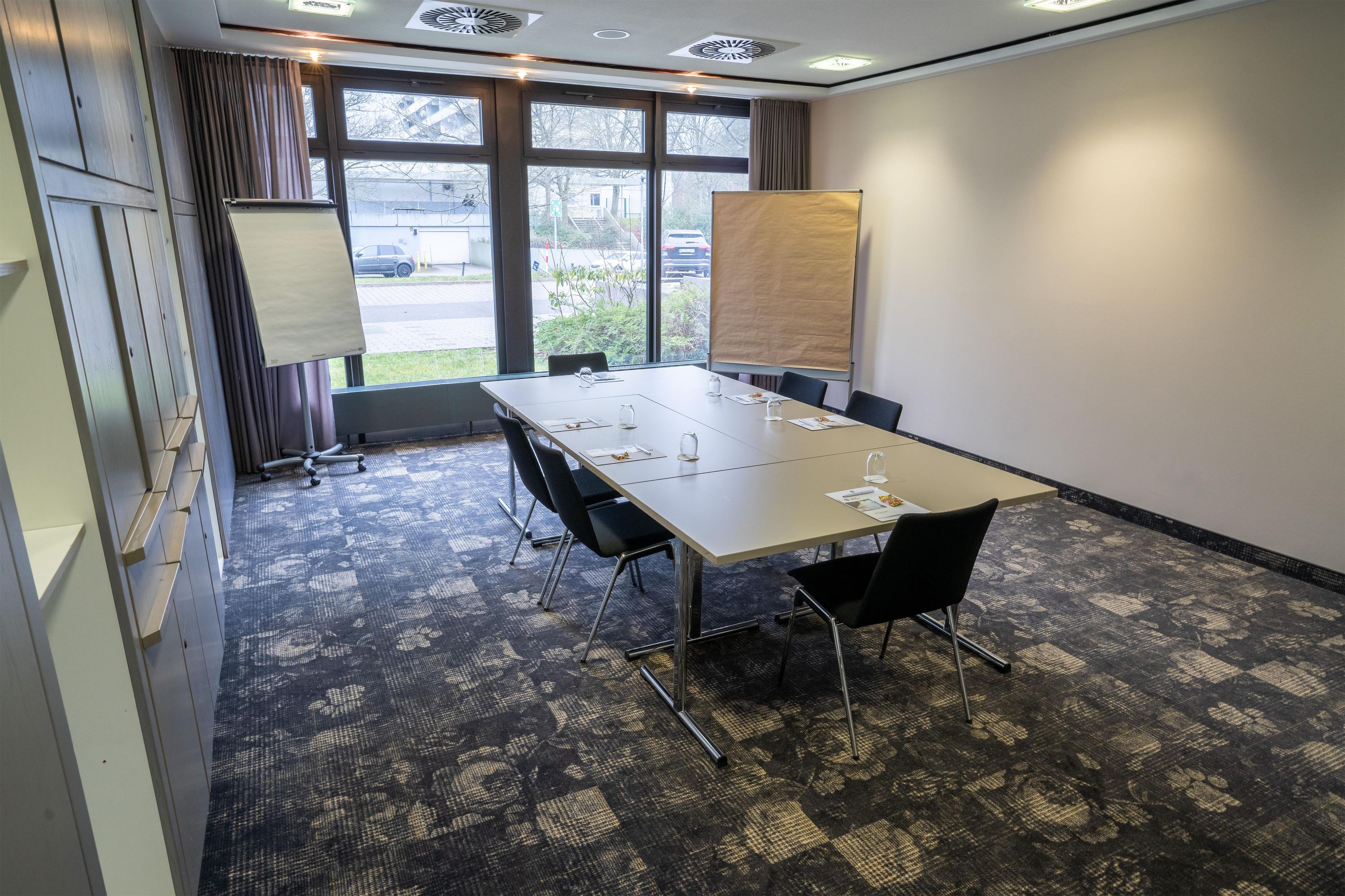 Un salón de conferencias con una gran mesa, sillas, una pantalla de proyector y vistas al exterior.