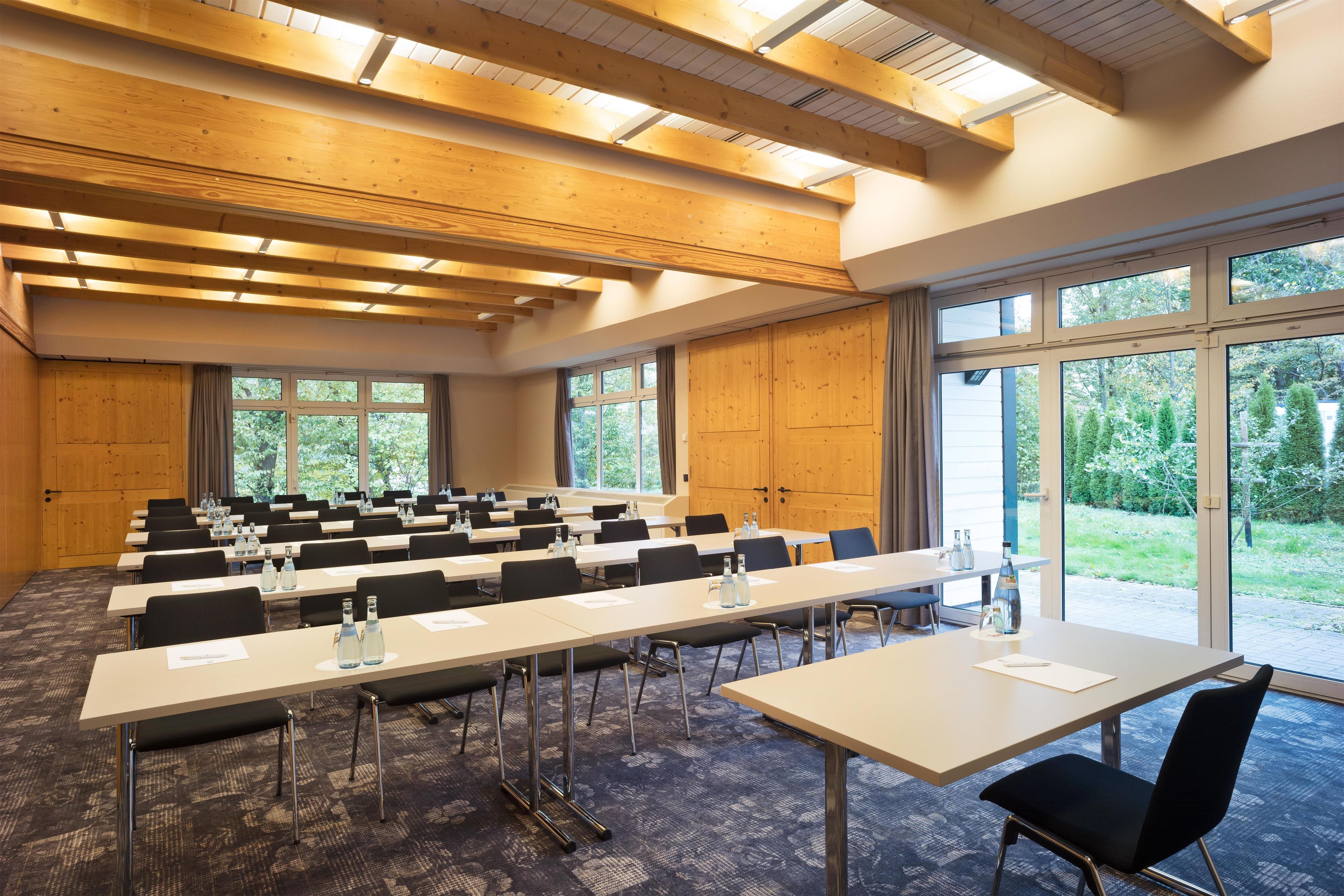 A conference room with multiple tables and chairs, large windows, and wooden ceiling beams.