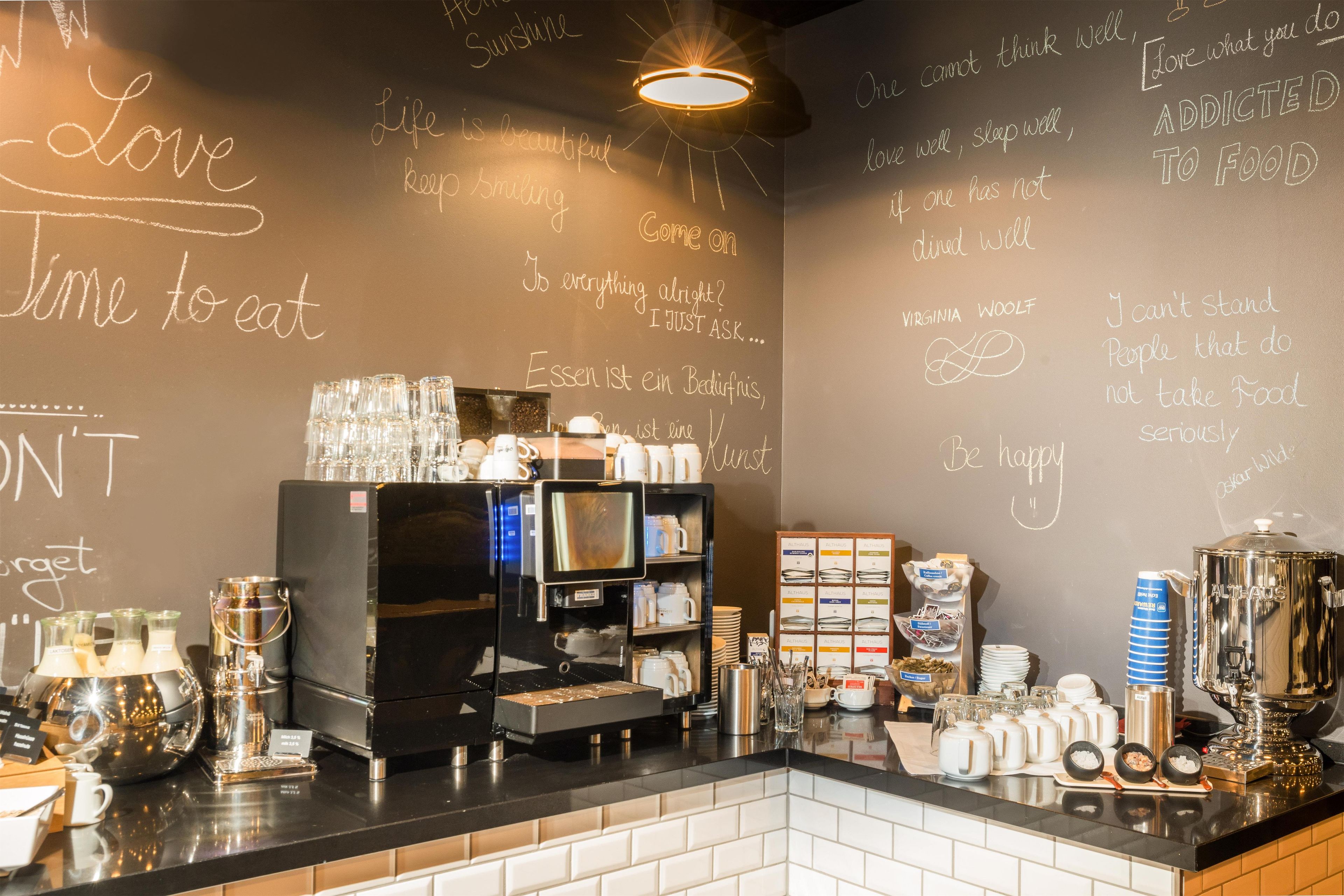 A café interior with a chalkboard wall displaying motivational phrases, a coffee machine, and various coffee cups and saucers.