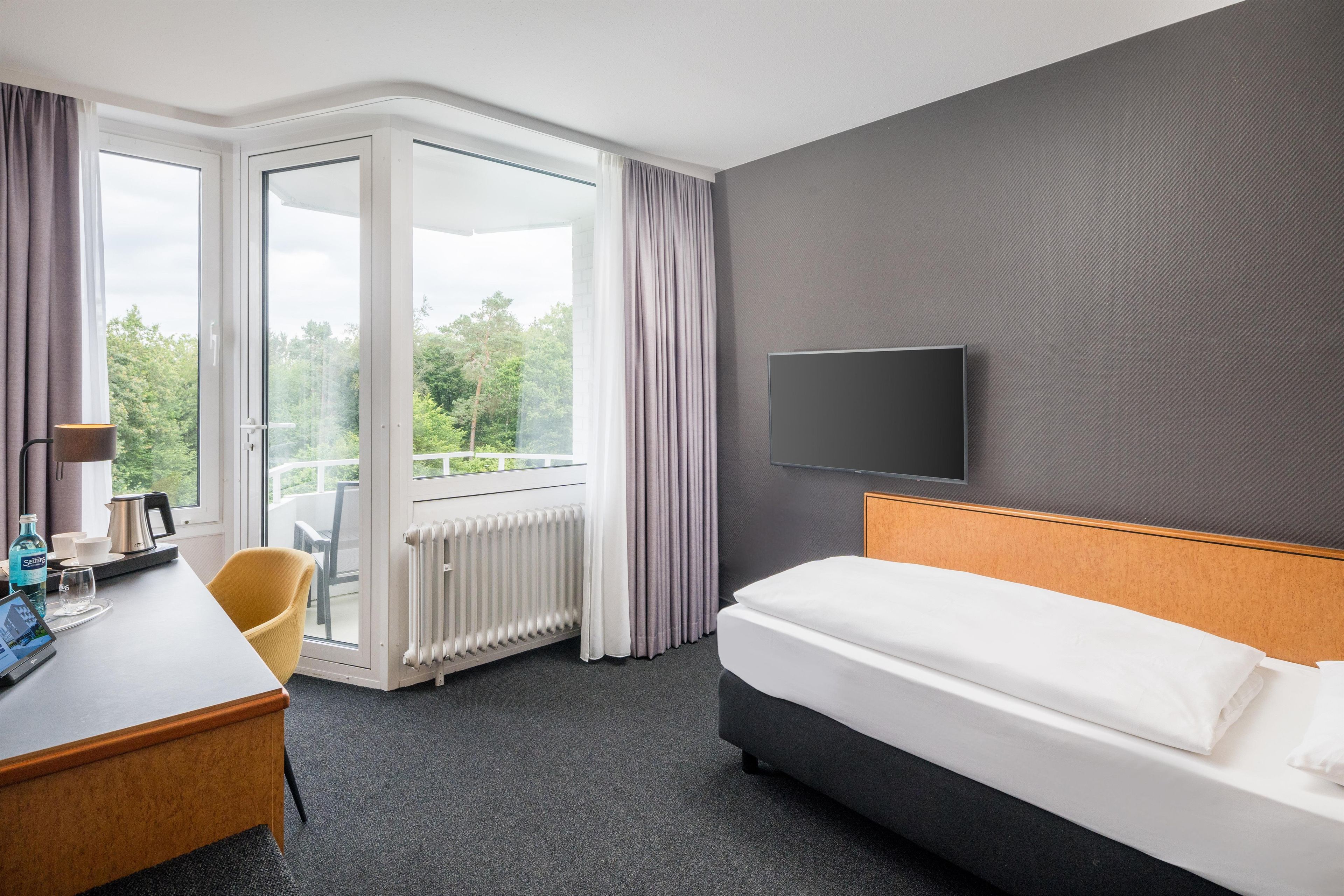 Habitación de hotel con cama, escritorio, silla, televisor y vistas al exterior.