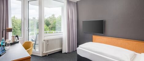 A hotel room with a bed, a desk, a chair, a TV, and a view of the outdoors.