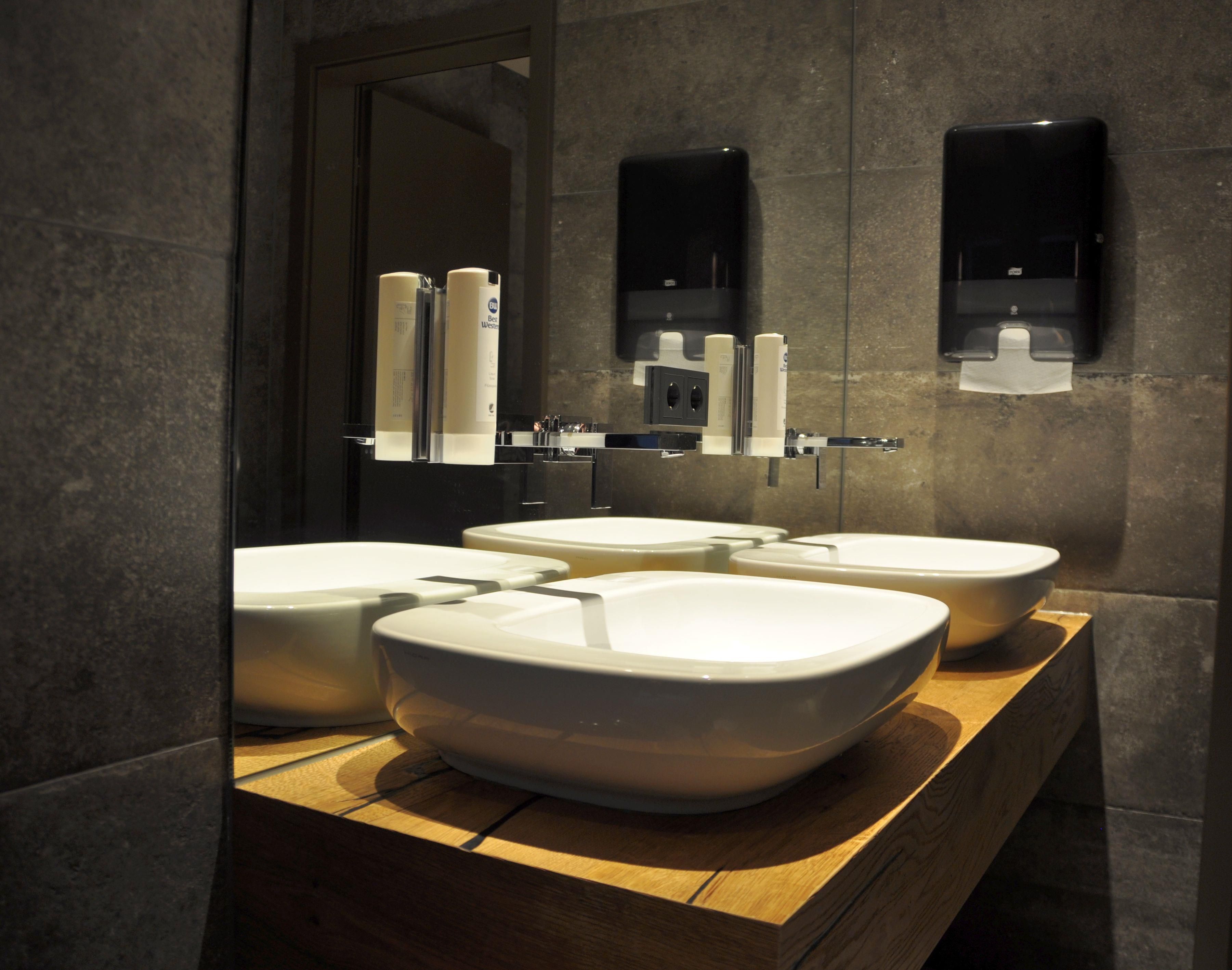 Un baño moderno con tres lavamanos, un espejo y dos dispensadores de jabón.