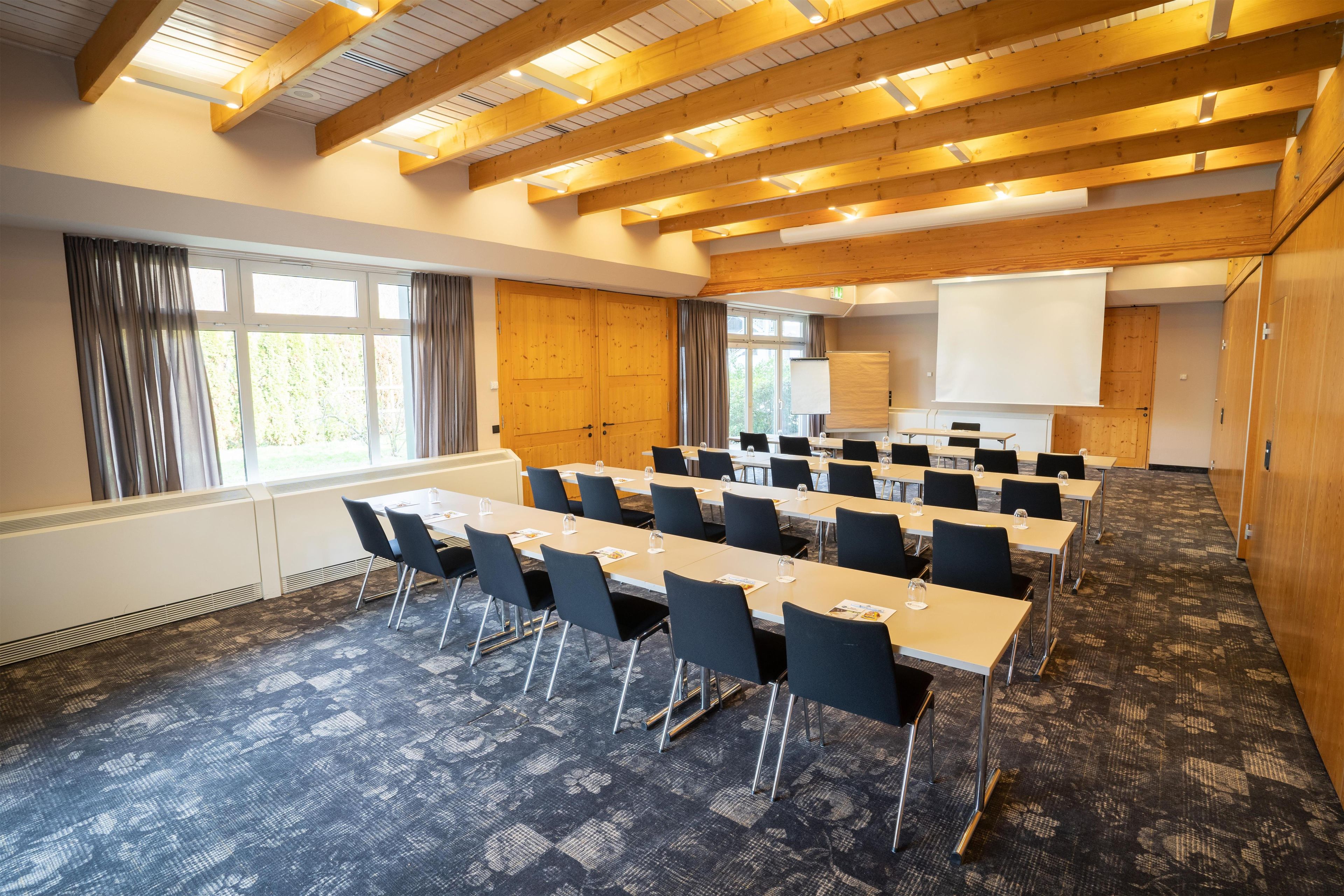 Un salón de conferencias con una larga mesa, sillas, una pantalla de proyector y un ventanal.