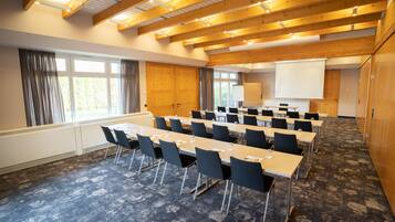 Un salón de conferencias con una larga mesa, sillas, una pantalla de proyector y un ventanal.
