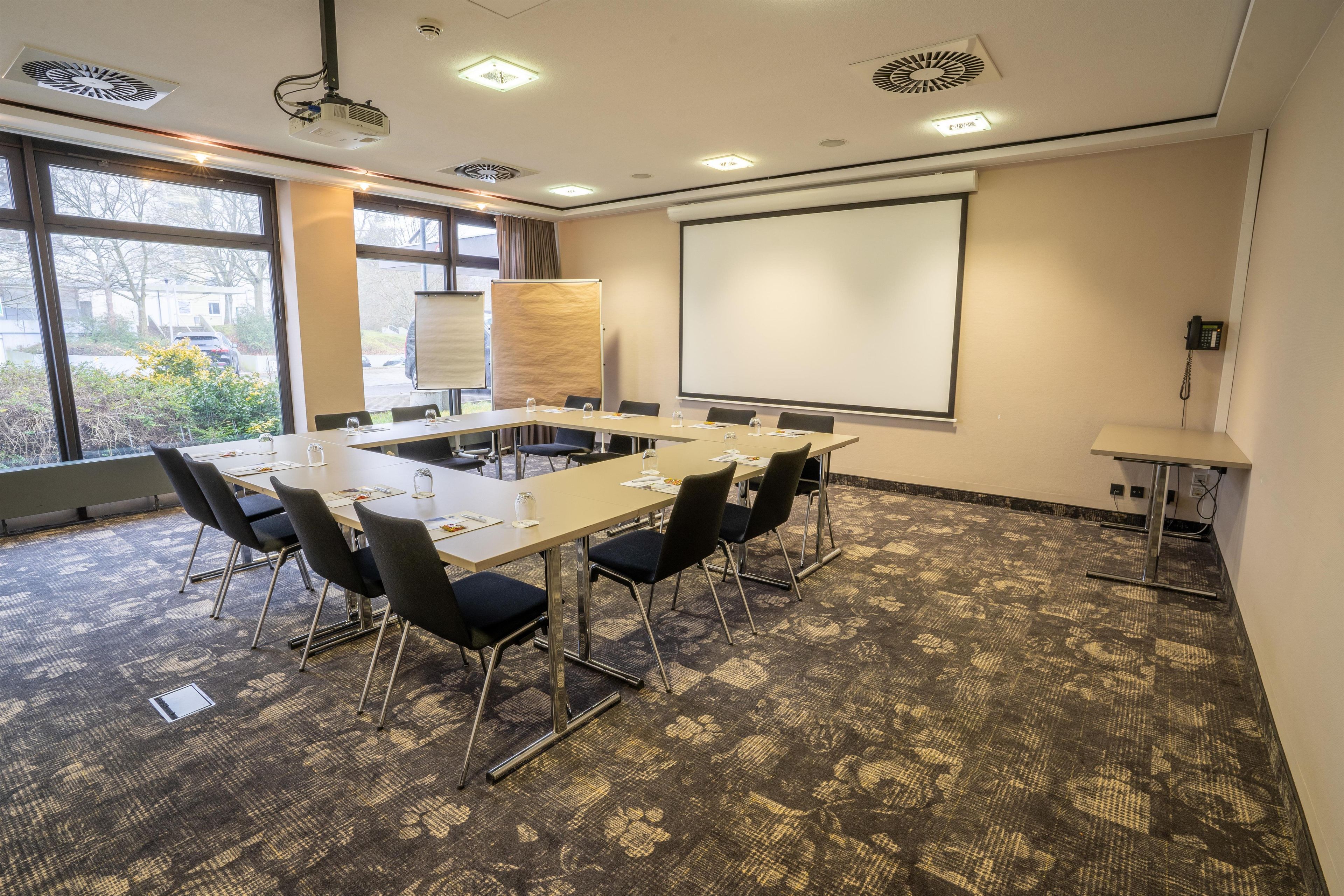 A conference room with a long table, chairs, a projector, a screen, and a whiteboard.