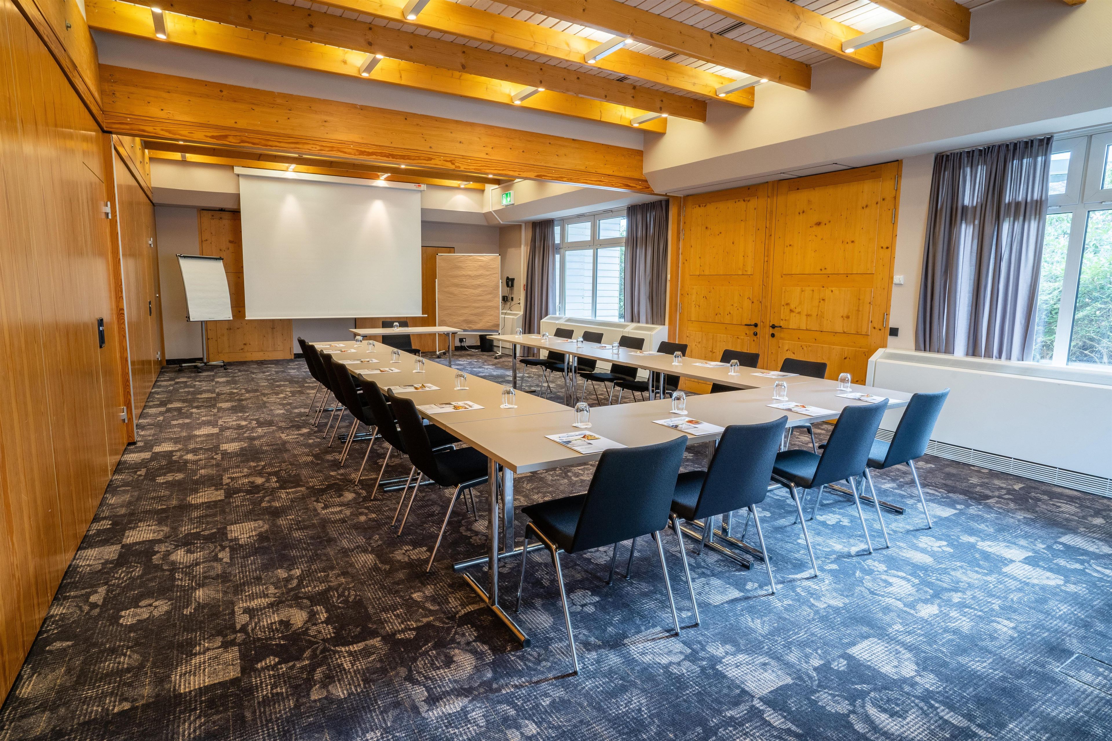 Un salón de conferencias con una larga mesa, sillas, una pizarra y una pantalla de proyector.