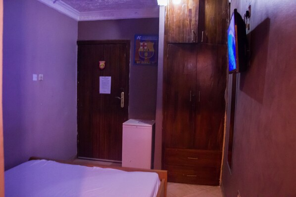 A room with a bed, a wardrobe, a small white cabinet, and a door with a coat of arms.