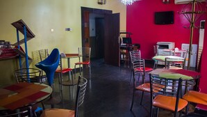 A restaurant with multiple tables and chairs, a television mounted on the wall, and a chandelier. - De Prince Guest House (Lagos)
