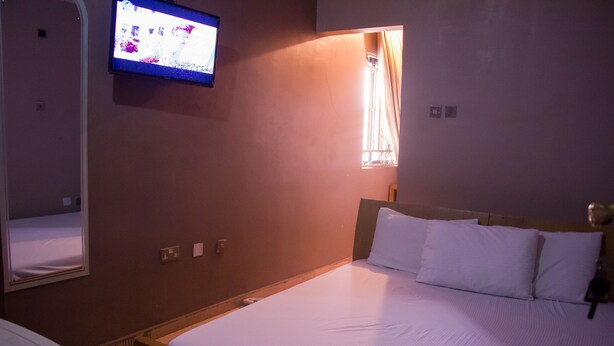 A hotel room with a bed, a television mounted on the wall, and a window with curtains. - De Prince Guest House (Lagos)