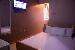 A hotel room with a bed, a television mounted on the wall, and a window with curtains.