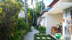 A pathway leading to a building with a white exterior, surrounded by lush greenery and a statue. - Villa Bau Nyale (Kuta)