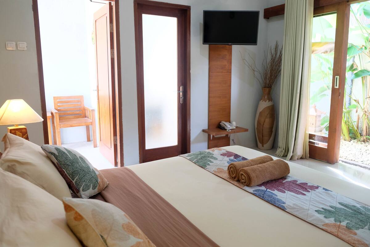 A hotel room with a bed, a chair, a TV, and a view of greenery.