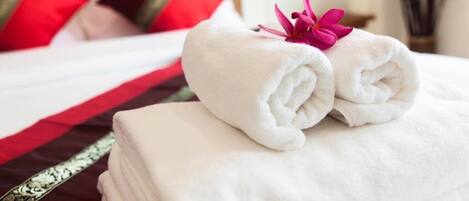 A neatly made bed with white and red bedding, a rolled white towel, and a pink flower.