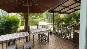 Een terras buiten met een tafel, stoelen, een grote parasol en uitzicht op een tuin.