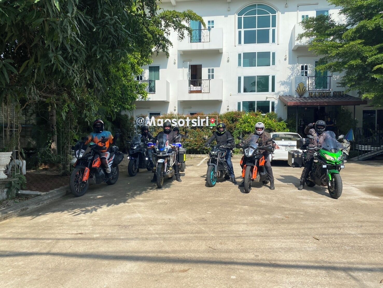 Eine Gruppe Motorradfahrer parkt vor einem Gebäude mit der Aufschrift "MAESOT SIRI".
