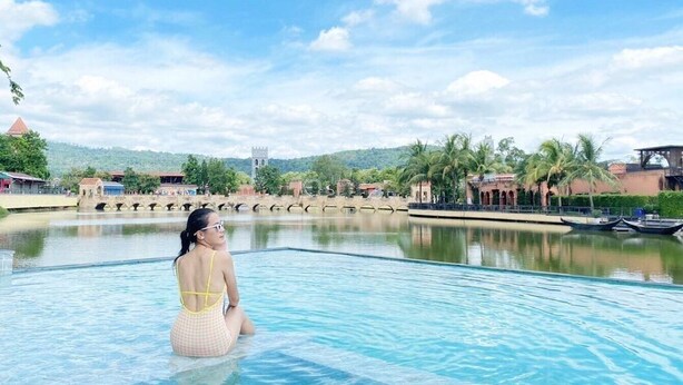 A woman sitting in a pool with a clear view of a bridge and buildings in the background.