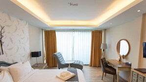 A hotel room with a large bed, a desk, a chair, a desk lamp, a mirror, and a television.