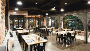 A restaurant with multiple tables and chairs, a brick wall, and large windows offering a view of the outdoors.