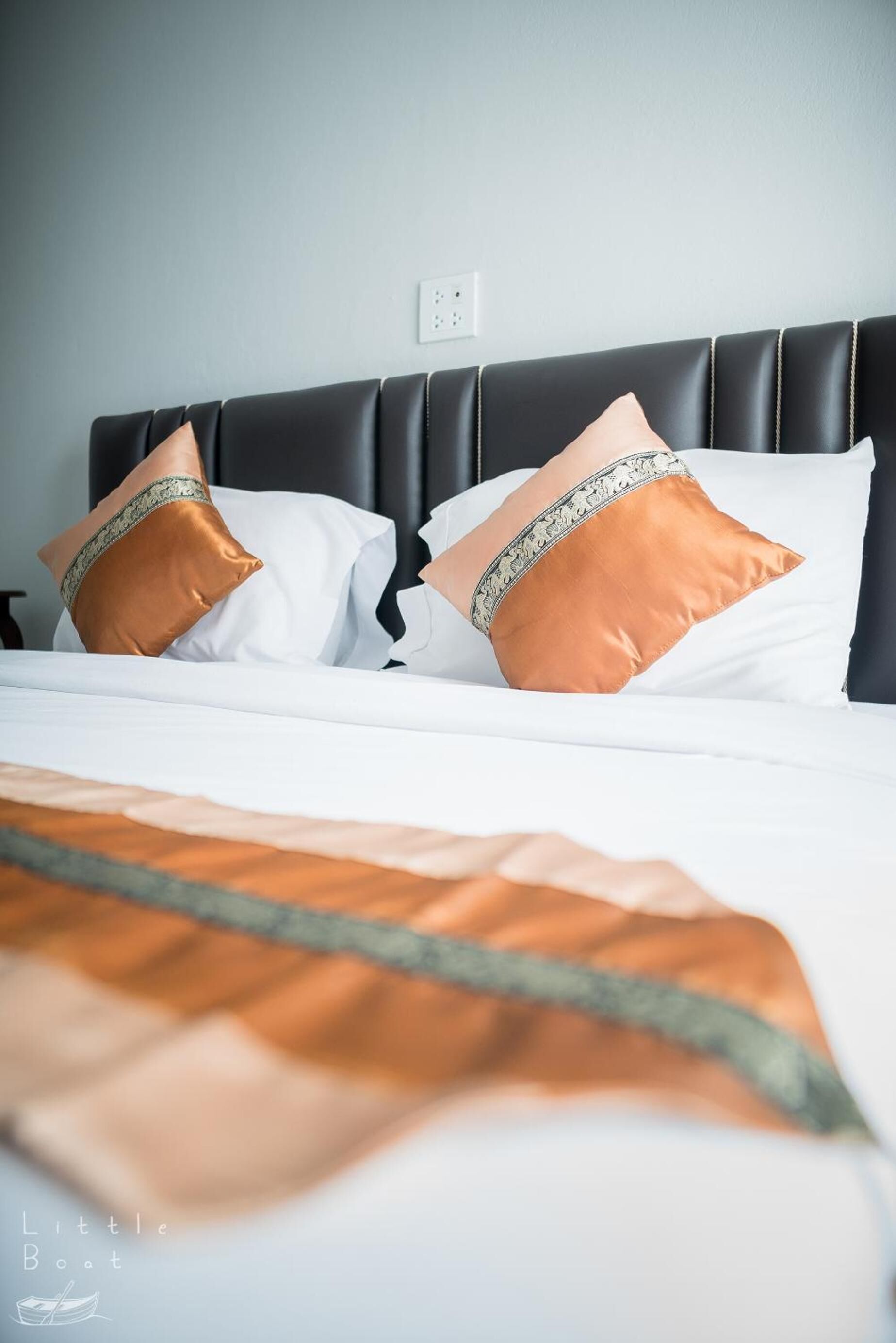 A neatly made bed with white linens and two decorative pillows, one with a gold and silver pattern and the other plain gold.