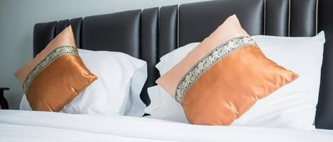 A neatly made bed with white linens and two decorative pillows, one with a gold and silver pattern and the other plain gold.
