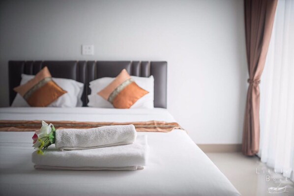 A neatly made bed with white linens and two decorative pillows, a folded towel, and a bouquet of flowers on the bed. - Retro Twin Home at Maesot (Mae Sot)