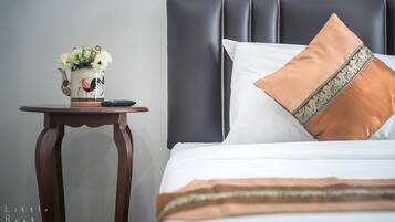 A neatly made bed with a white and brown pillow, a decorative vase with flowers, and a remote control on a wooden nightstand.