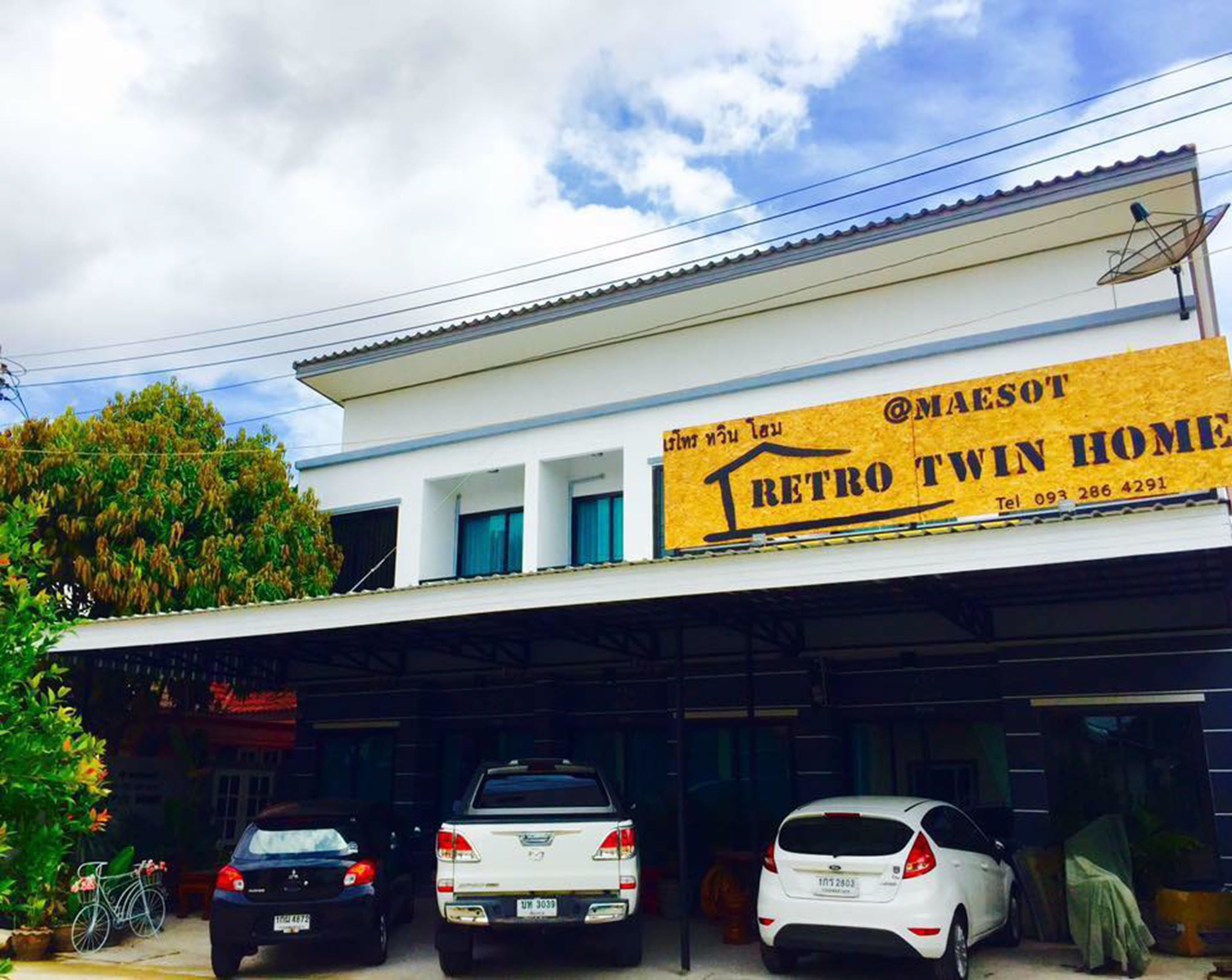 Un edificio con un cartel que anuncia 'RETRO TWIN HOME' y un número de contacto. Hay tres coches estacionados adelante.