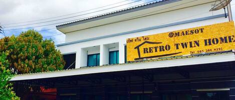 Un edificio con un cartel que anuncia 'RETRO TWIN HOME' y un número de contacto. Hay tres coches estacionados adelante.