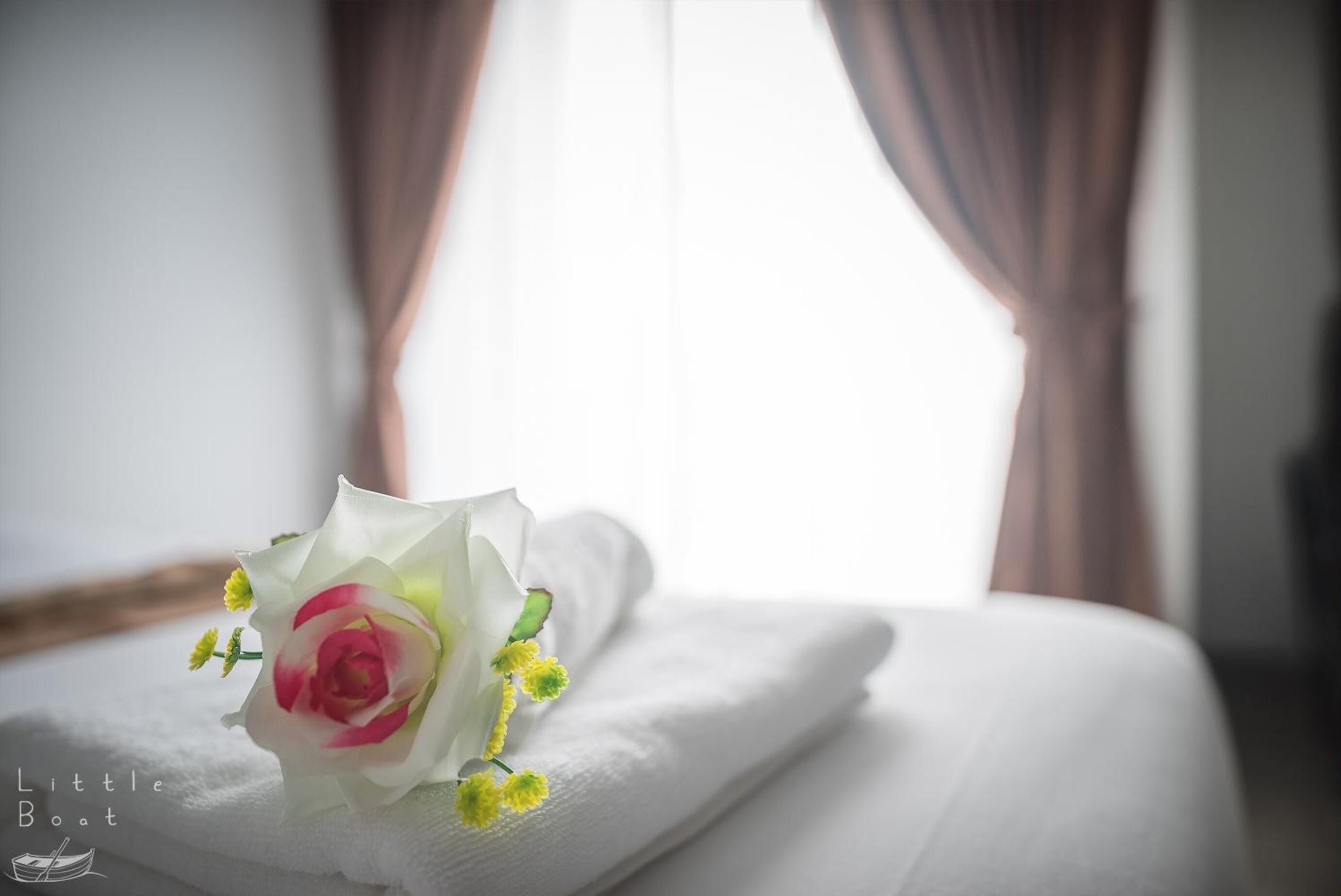 A neatly made bed with a white pillow and a bouquet of flowers on it.