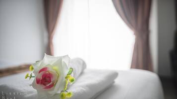A neatly made bed with a white pillow and a bouquet of flowers on it.