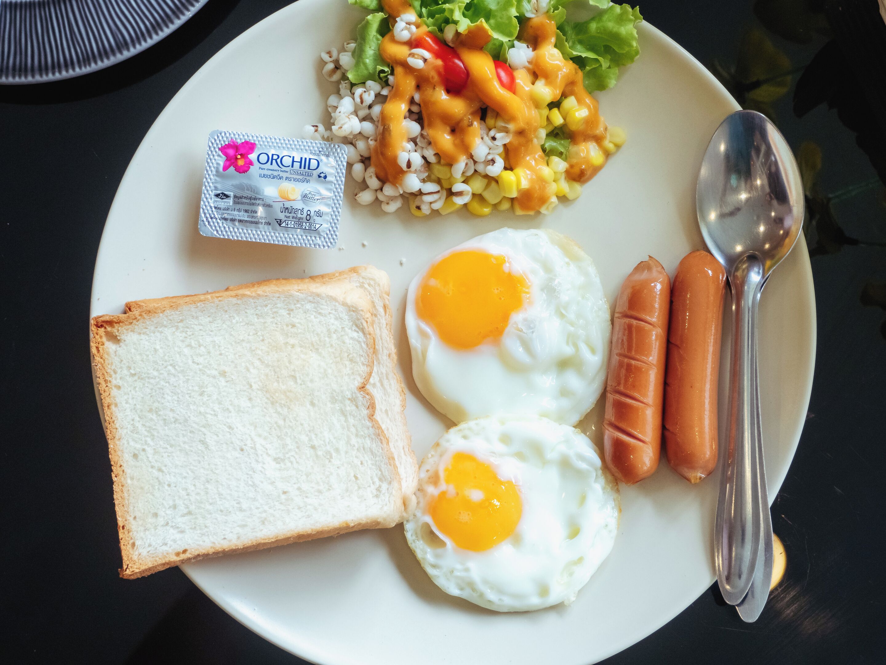 Un plato con huevos, salchicha, tostadas y una ensalada.