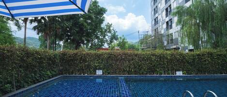 Una piscina con pavimento in piastrelle blu, circondata da un siepe e un edificio sullo sfondo.