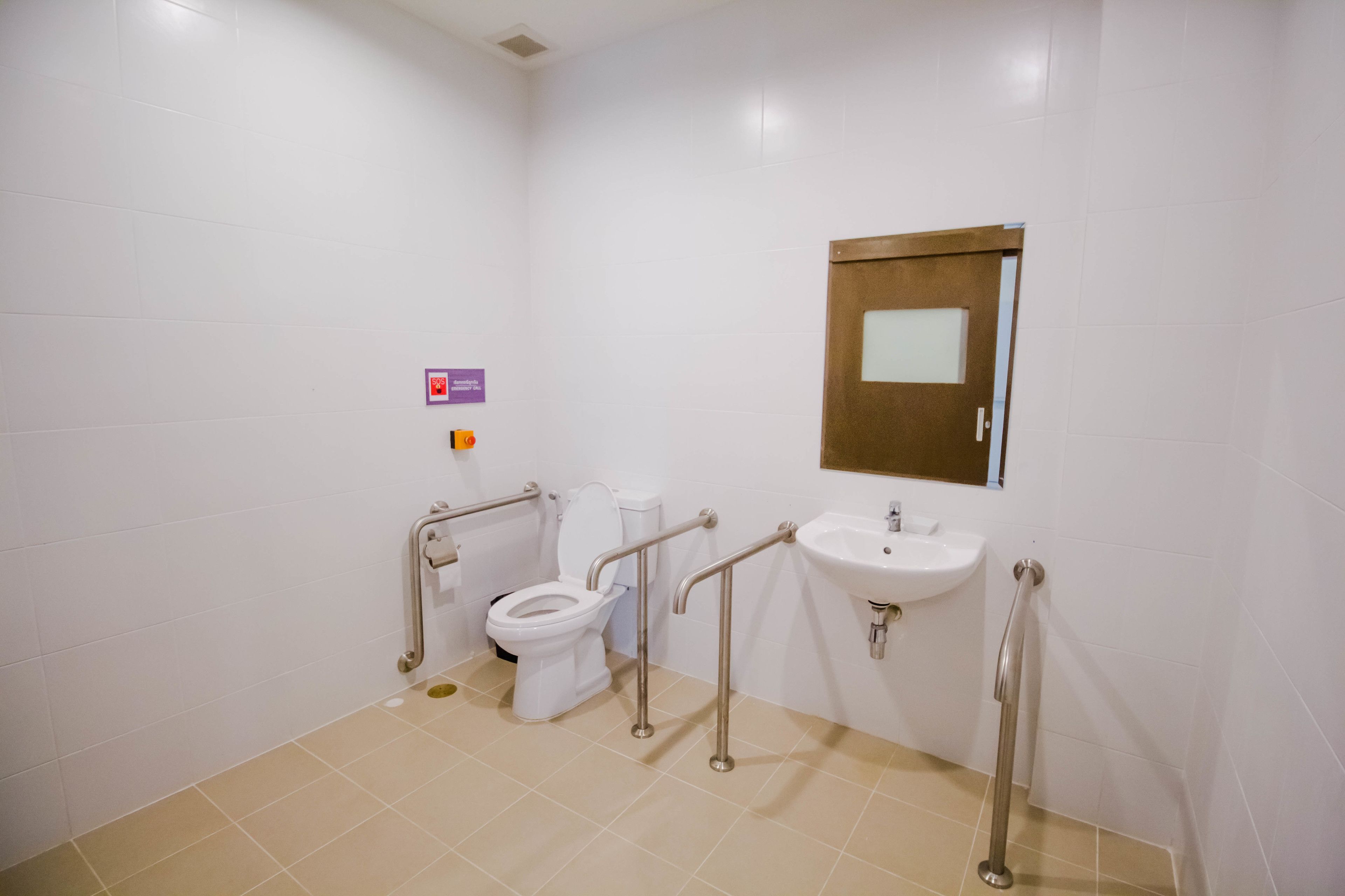 A bathroom with white tiles, a toilet, a sink, and handrails.