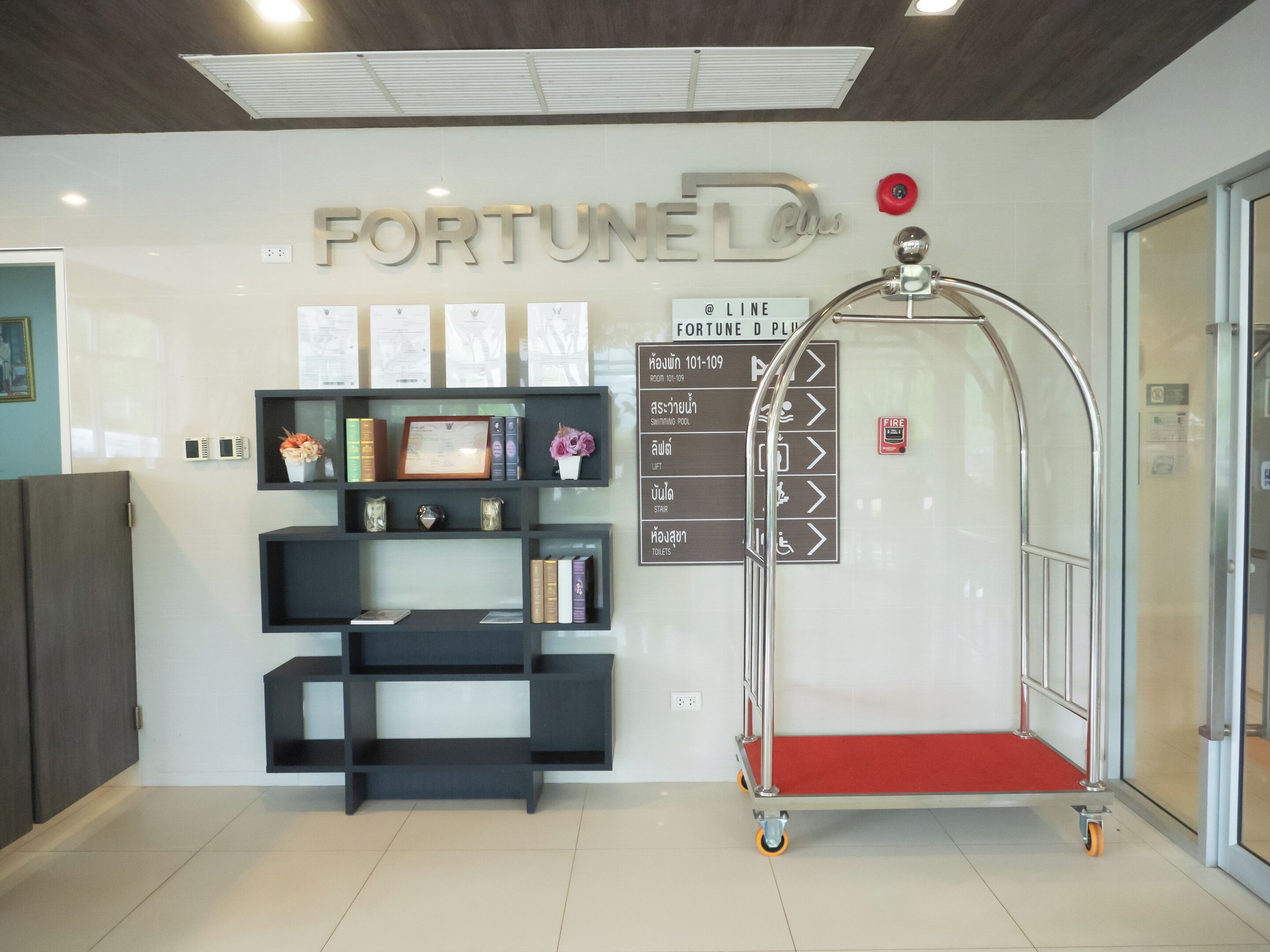 Un espace d’accueil avec un panneau indiquant « FORTUNE D’ », un bureau, une bibliothèque, un détecteur d’incendie et des panneaux de signalisation.
