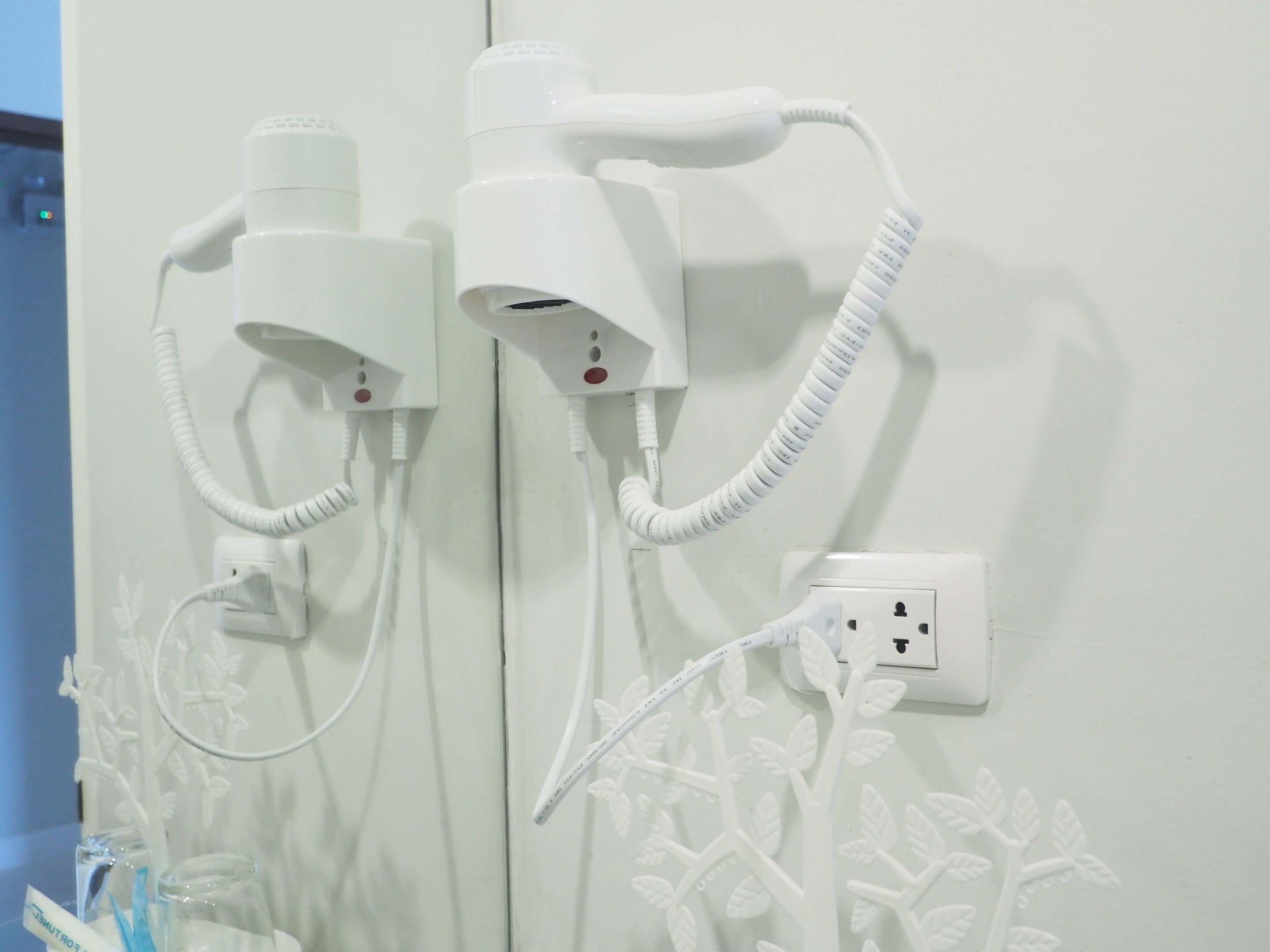 A bathroom with two hair dryers mounted on the wall, connected to a power outlet.