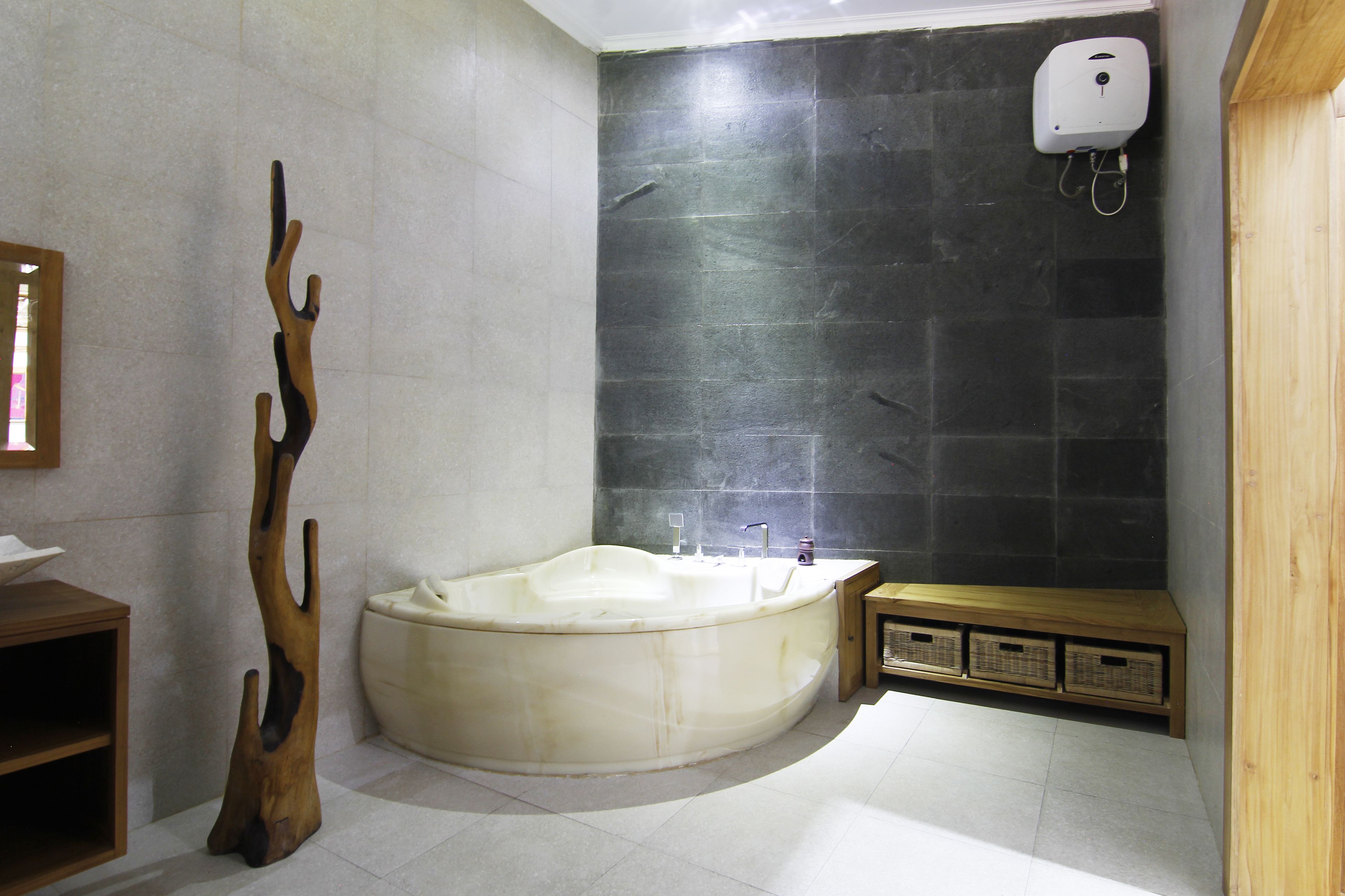 A modern bathroom with a freestanding bathtub, a wooden sculpture, a wooden bench, and a wall-mounted soap dispenser.