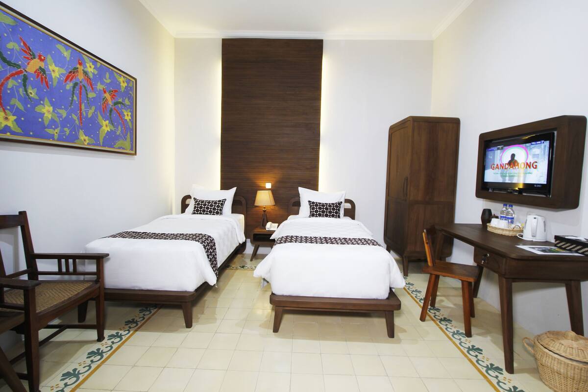 Une chambre d’hôtel avec deux lits, un bureau, une télévision et un tableau au mur.